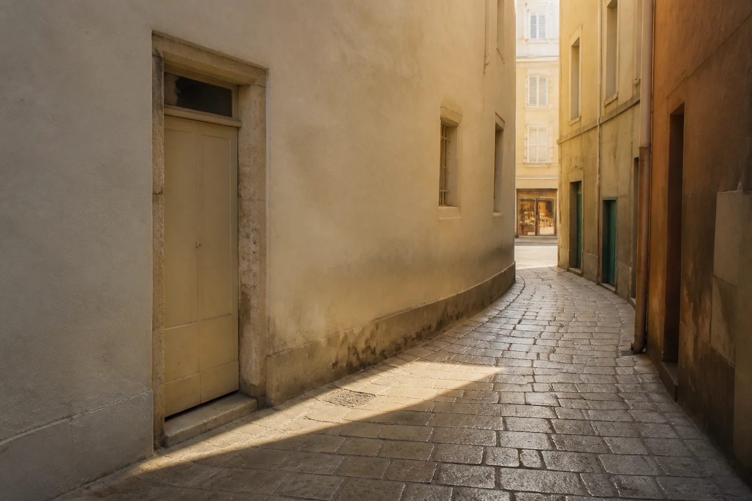 Narrow side street turning away from a brighter main line, plaster walls and a workshop door, soft shadow across worn paving stones, 1600x1000
